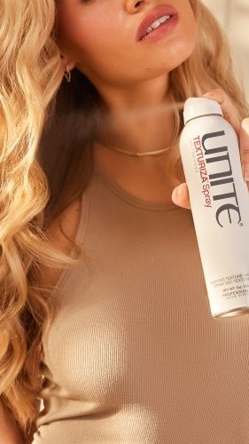Model holds Unite Texturiza Spray near styled waves, highlighting touchable texture, definition and professional finishing benefits