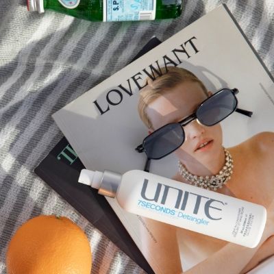 Flat lay of UNITE 7Seconds Detangler on a magazine with sunglasses and citrus, styled for hair care inspiration