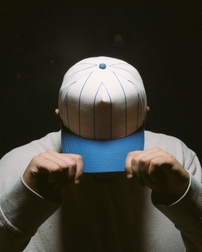 Person adjusting white pinstripe cap with blue brim under spotlight