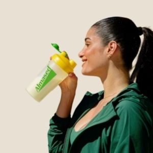 Woman drinking a nutrition shake from an Almased shaker bottle outdoors