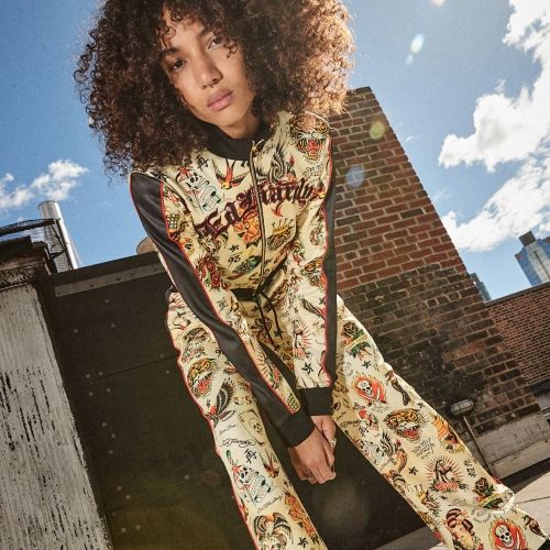 Woman posing in a cream Ed Hardy printed tracksuit featuring vintage tattoo graphics and sporty styling