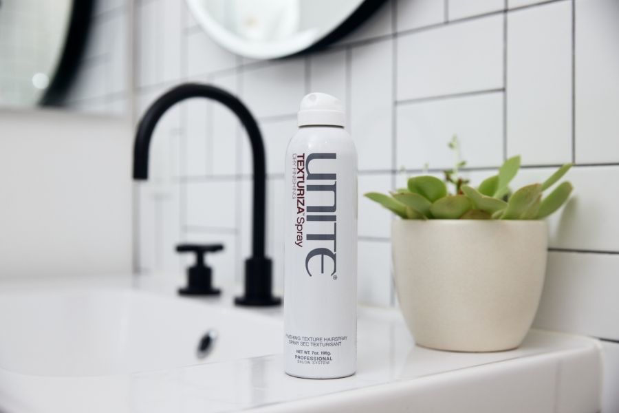 UNITE Texturiza dry finishing texture spray canister on bathroom counter with succulent, sink, and black faucet