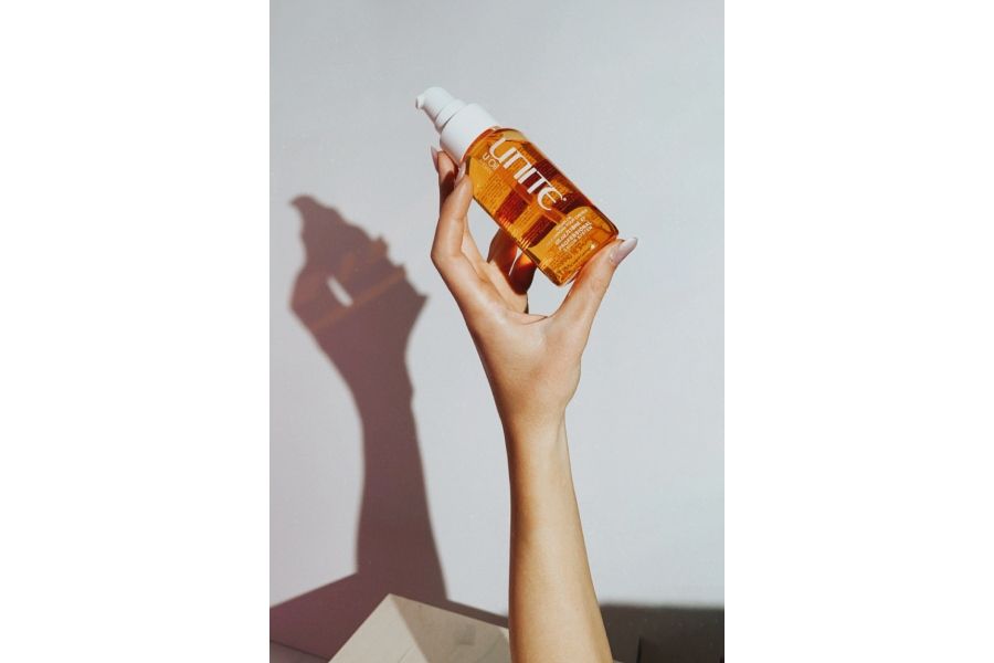 Hand holding amber UNITE HAIR U Oil bottle with pump, highlighting argan oil for smooth shine.