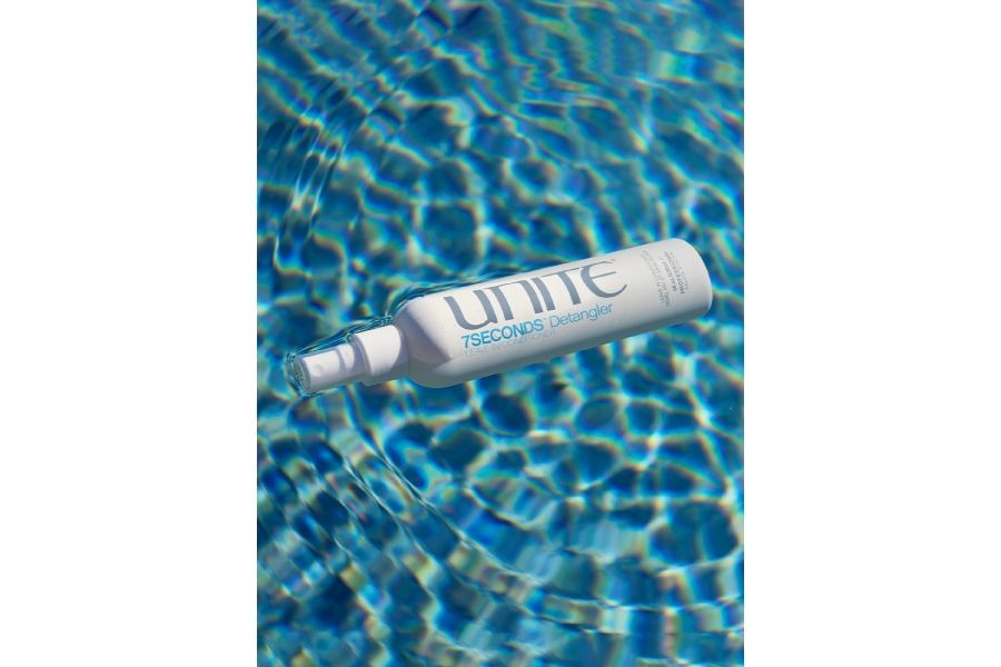 White UNITE HAIR 7SECONDS Detangler spray bottle floating in clear rippling blue water with fresh aesthetic.