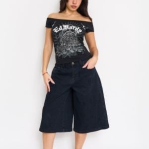 Woman wearing black off-shoulder Ed Hardy graphic top with wide-leg dark denim shorts.