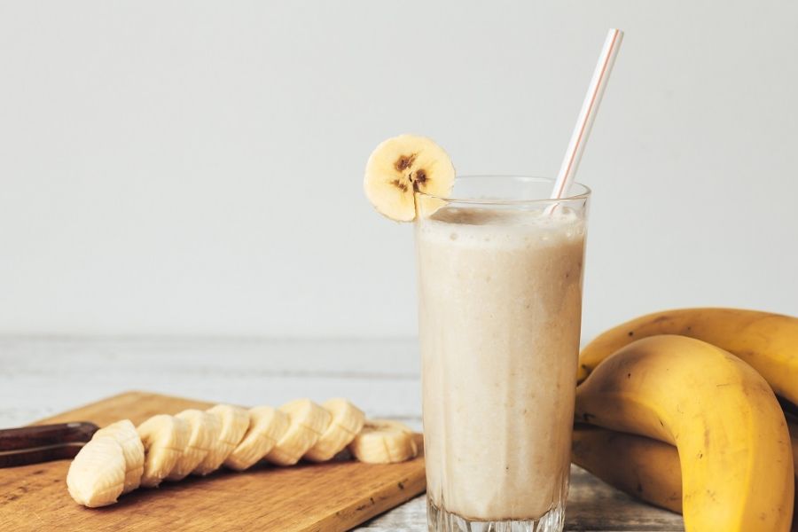 Almased banana smoothie in glass with garnish beside sliced and whole bananas, highlighting natural ingredients and healthy nutrition