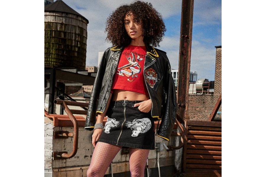 Woman in black leather jacket, red Ed Hardy crop tee, and tiger-print denim skirt with fishnets on a rooftop